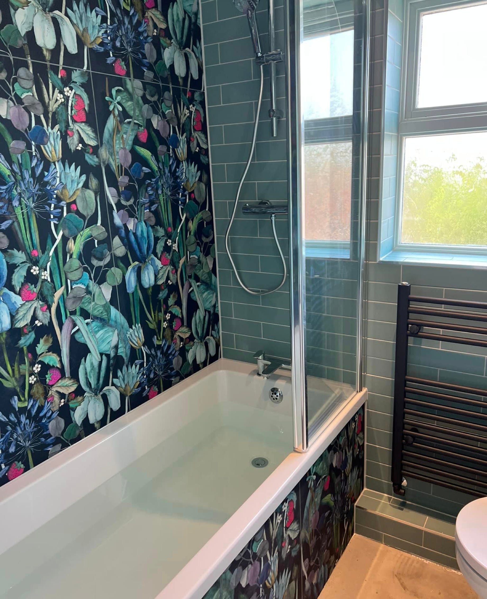 Image of bath with modern blue decorative floral tiles on the wall and bath side with an adjacent wall of plain aqua tiles with a modern fitted radiator.