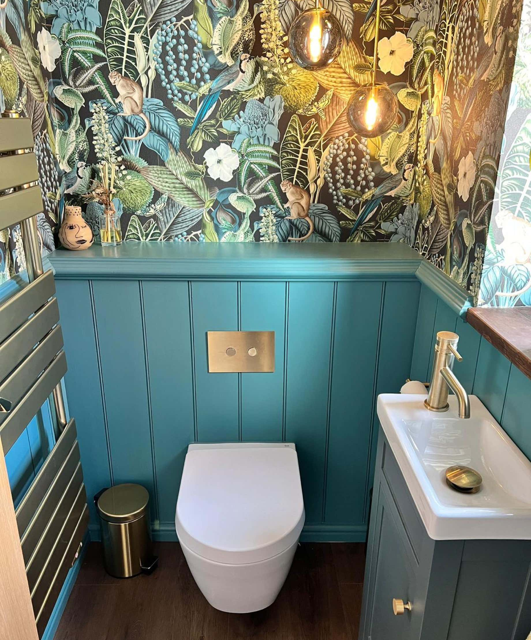 Image of downstairs w/c with water resistant floral wallpaper, a back-to-wall pan style toilet with a concealed cistern and flush plate, a boxed off rear unit and a slimline water basin housed in an under-sink cupboard.