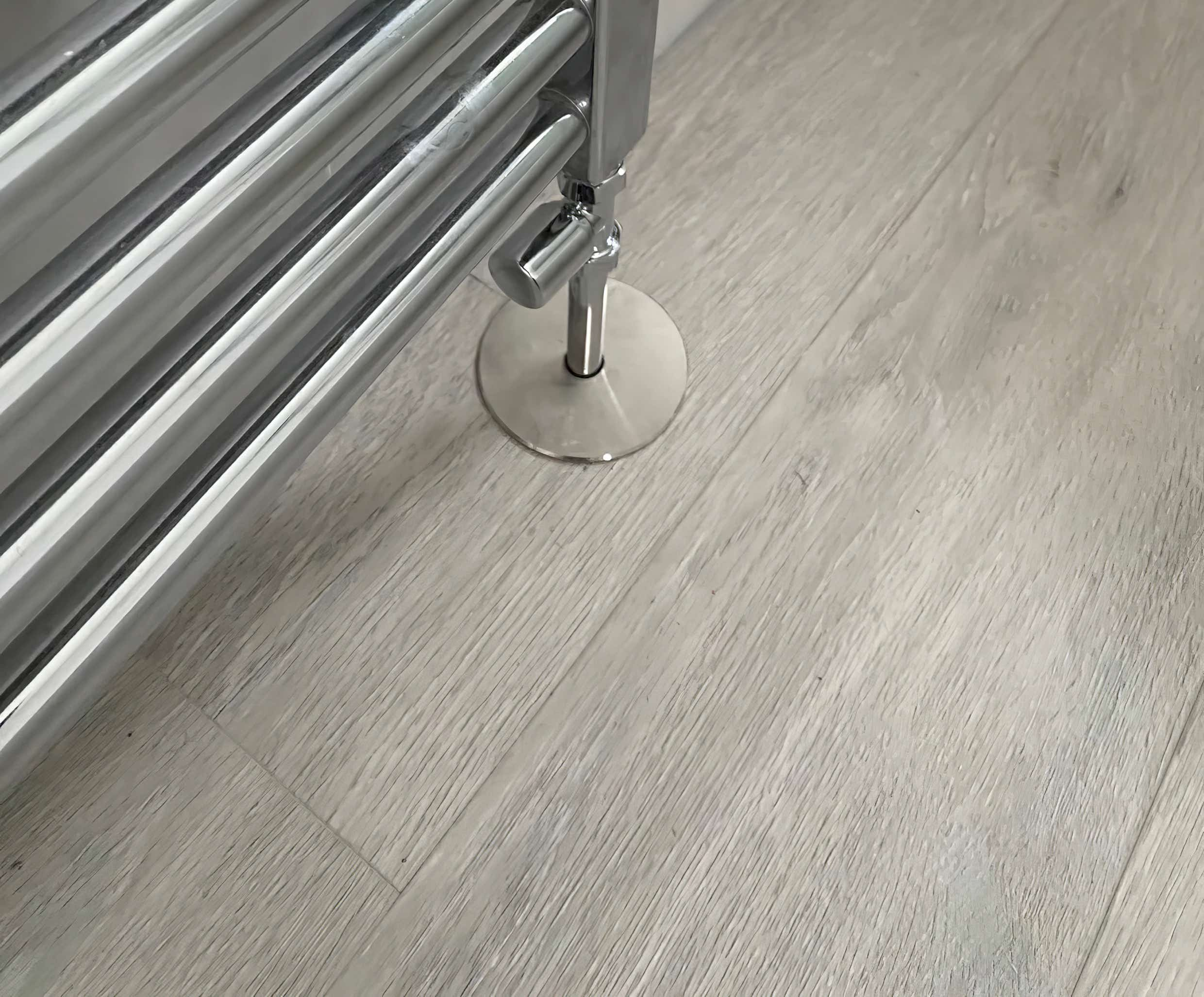 Image of chrome vertical radiator aspect on woodgrain pattern lvt flooring beautifully installed by Plumb Yorkshire Ltd.