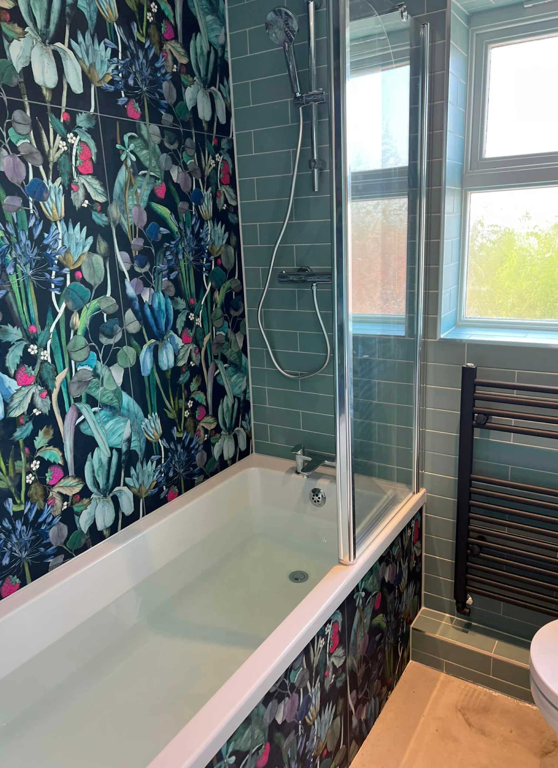 Image of bath with modern blue decorative floral tiles on the wall and bath side with an adjacent wall of plain aqua tiles with a modern fitted radiator.