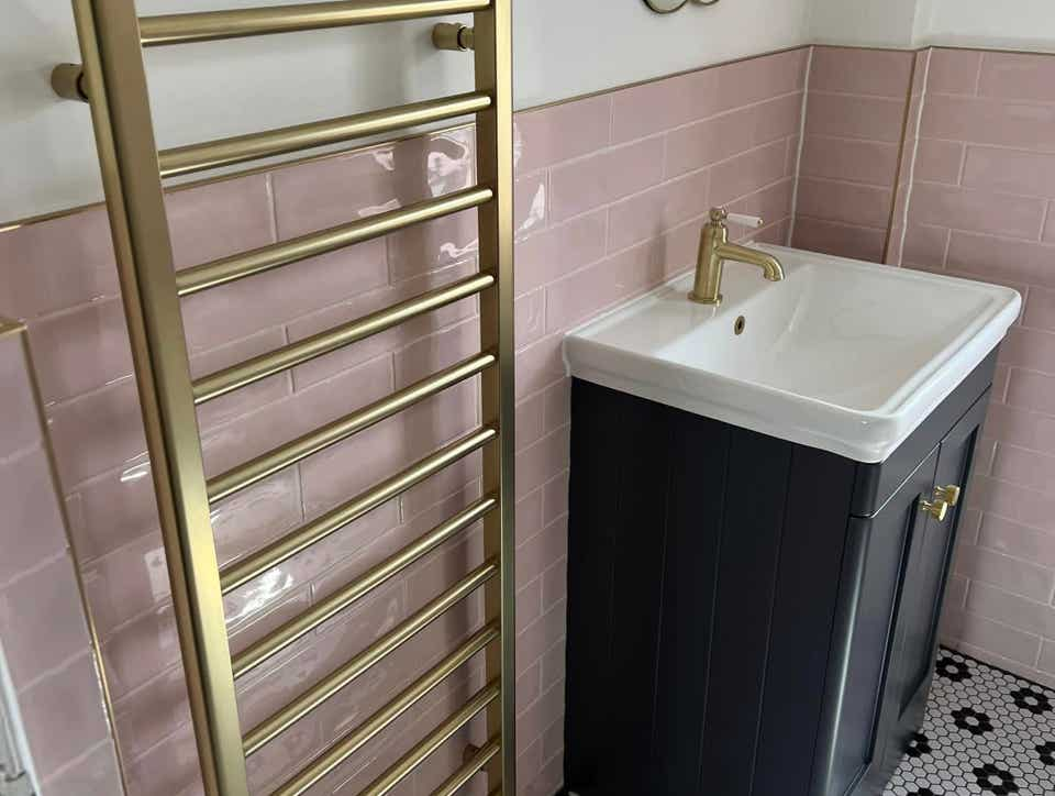 Image of a modern bathroom with pink brick layout tiles. brushed gold style fittings with black and white hexagon floor tiles installed by Plumb Yorkshire Ltd.